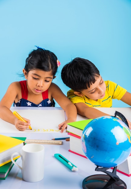 Lindas crianças indianas ou asiáticas estudando na mesa de estudo com uma pilha de livros, globo educacional, isolado sobre a cor azul claro