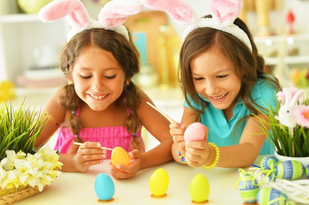 Lindas dos hermanas con orejas de conejo decorando huevos de Pascua