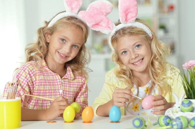 Lindas dos hermanas con orejas de conejo y pintando huevos de Pascua en casa