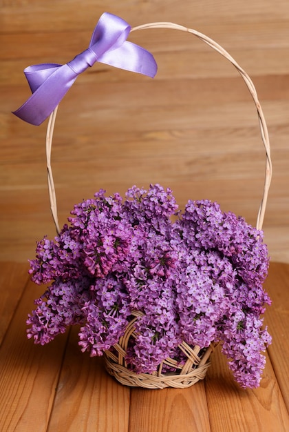 Lindas flores de lilás em cesta de vime na mesa em fundo de madeira