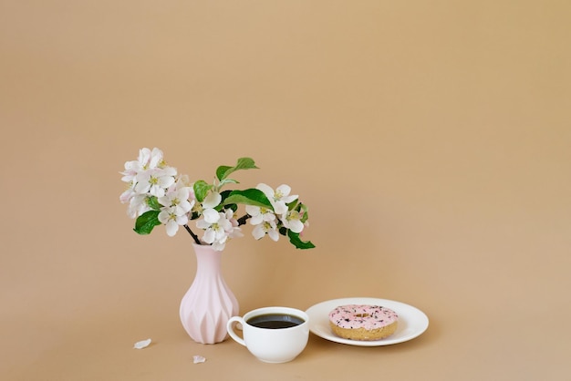 Lindas flores de macieira branca em rosquinhas de vaso branco e uma xícara de chá em um fundo bege com um espaço de cópia