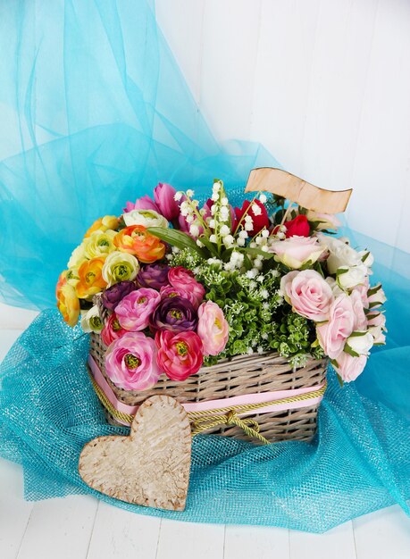Lindas flores na cesta de vime, em tecido colorido e fundo de madeira
