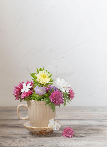 Foto lindas flores na taça na mesa de madeira na parede branca de fundo