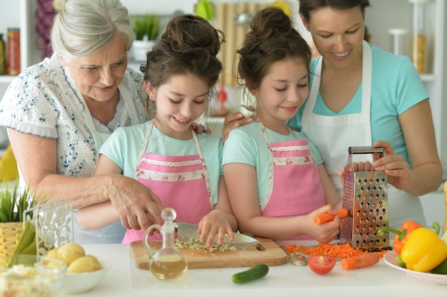 Lindas garotas com mãe e avó preparando deliciosa salada fresca na cozinha