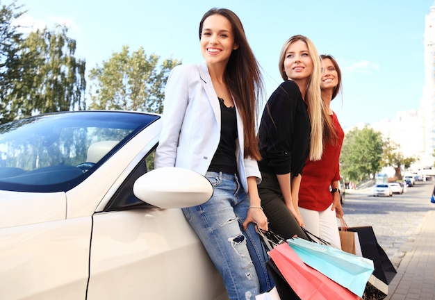 Lindas garotas com sacolas de compras discutindo compras e sorrindo enquanto se inclinam sobre o carro