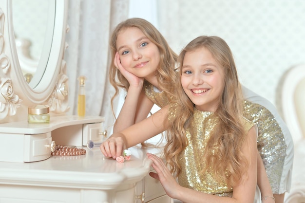 Lindas hermanas gemelas sonrientes con brillantes vestidos dorados sentadas cerca del tocador