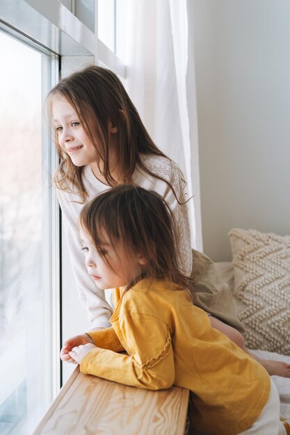 Lindas hermanitas mirando por la ventana en casa