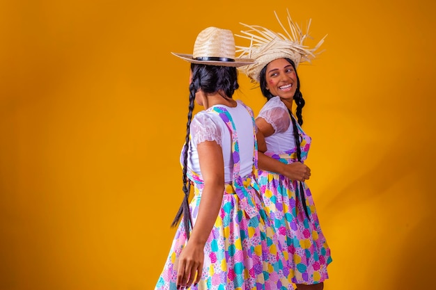 Foto lindas irmãs gêmeas vestindo roupas tradicionais para festa de junho dançando em fundo amarelo