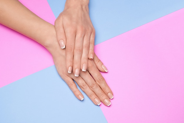 Lindas mãos femininas com manicure francesa sobre superfície de papel colorido