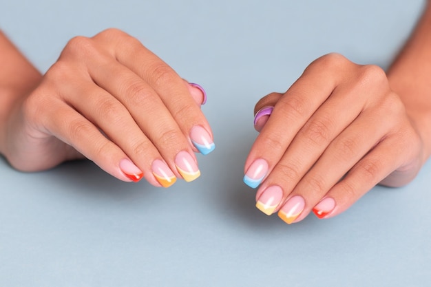 Lindas mãos femininas com unhas coloridas de manicure com desenho de arco-íris