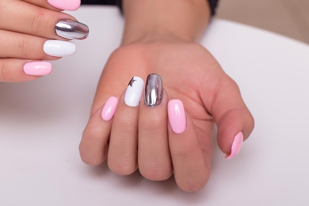 Lindas mãos femininas com unhas coloridas de manicure, esmalte de gel cor de rosa e prata