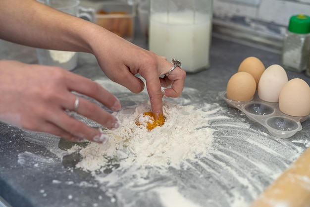 Lindas mãos femininas quebram ovos em farinha para amassar uma bela massa Conceito de culinária