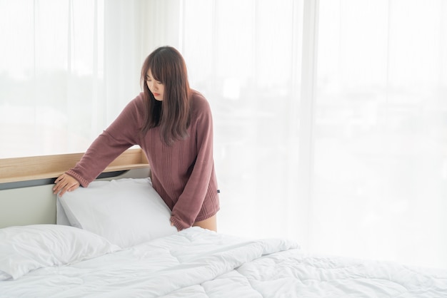 lindas mulheres asiáticas fazendo a cama em quarto com lençol branco limpo