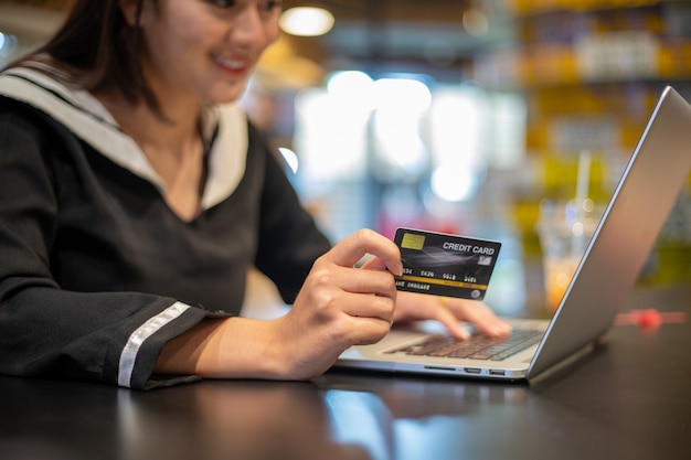 Lindas mulheres asiáticas segurando um cartão de crédito e um telefone celular para fazer compras online. ela sorrindo e feliz