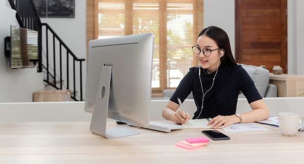 Lindas mulheres asiáticas trabalham e se encontram on-line em casa por meio de computadores. Interagindo com colegas Com um rosto feliz e sorridente, uma nova atividade online normal