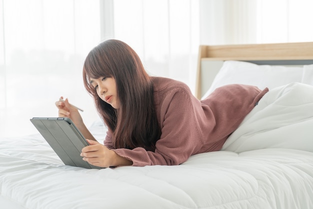 Lindas mulheres asiáticas trabalhando com tablet na cama