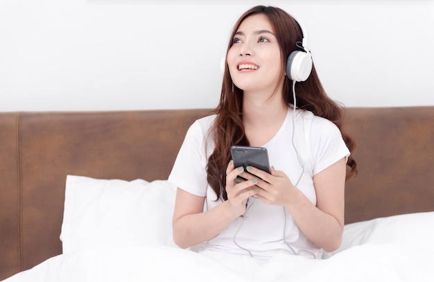 Lindas mulheres asiáticas usando fones de ouvido, ouvindo música em streaming de seus smartphones.