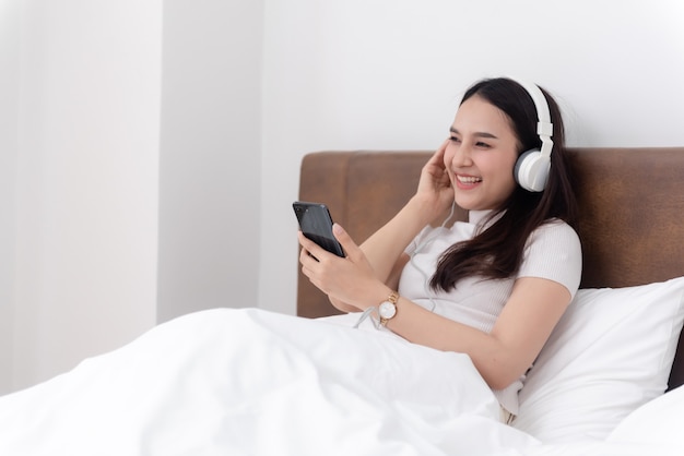 Lindas mulheres asiáticas usando fones de ouvido, ouvindo música em streaming de seus smartphones.