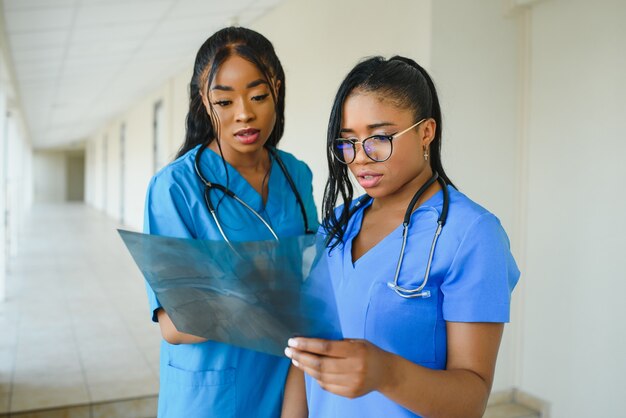 Lindas mulheres e lindos médicos afro-americanos examinando uma fotografia de raio-X, dois outros médicos conversando ao fundo