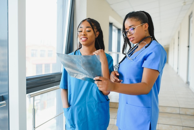 Foto lindas mulheres e lindos médicos afro-americanos examinando uma fotografia de raio-x, dois outros médicos conversando ao fundo