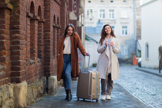 lindas namoradas com uma mala e fazendo compras dão um passeio pela cidade em busca de um hotel