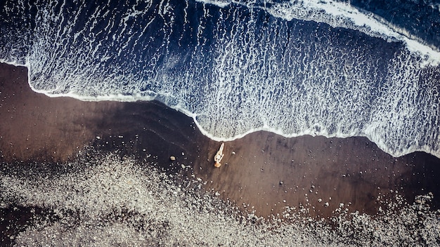 Lindas pessoas caucasianos modelam na praia em tenerife, pegando sol enquanto uma grande onda vem até ela. conceito aéreo de férias com drone. meditação e alegria para um estilo de vida independente
