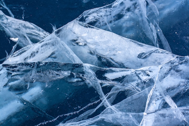 Lindas rachaduras no gelo espesso e claro do lago. Gelo transparente azul com rachaduras brancas. Horizontal.
