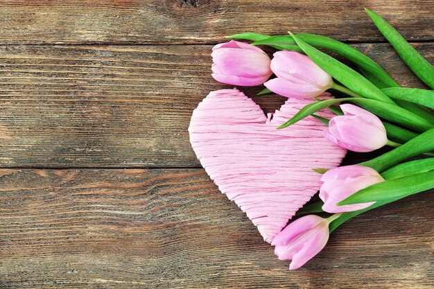 Lindas tulipas cor de rosa com coração decorativo em fundo de madeira