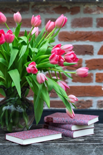 Lindas tulipas cor de rosa em um vaso e livros contra um fundo de parede de tijolos