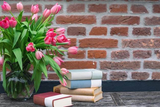 Lindas tulipas cor de rosa em um vaso e livros contra um fundo de parede de tijolos