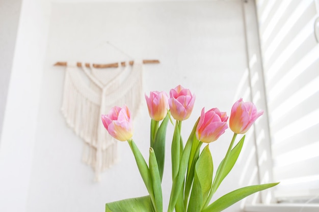 Lindas tulipas cor-de-rosa em vaso de vidro contra macrame artesanal pendurado na parede ECO conceito moderno amigável no interior