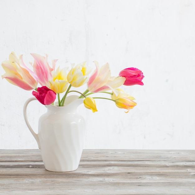 Lindas tulipas em uma jarra branca em fundo de madeira
