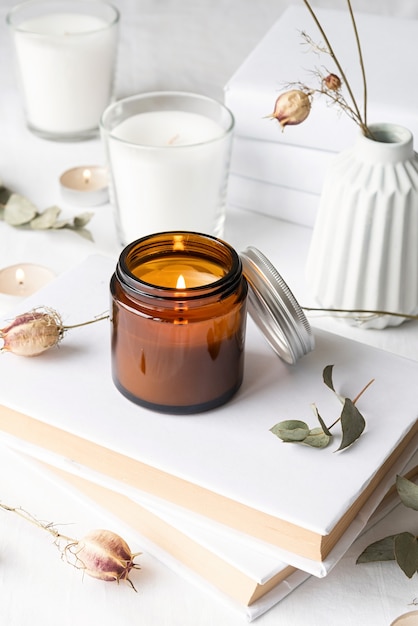 Lindas velas acesas com folhas de eucalipto e flores secas em uma pilha de livros brancos