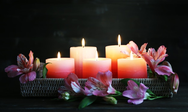 Lindas velas com flores na mesa de madeira, em fundo escuro