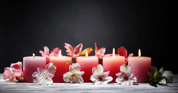 Lindas velas com flores na mesa de madeira, em fundo escuro