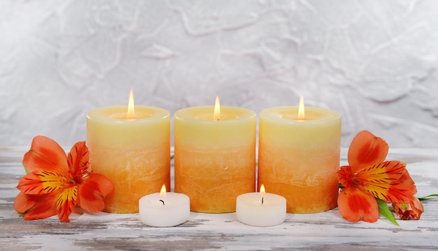 Lindas velas com flores na mesa em fundo cinza