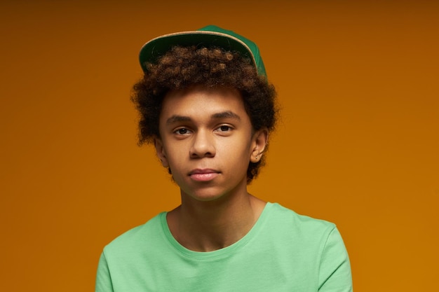 Lindo adolescente con expresión facial neutra con camiseta verde y gorra