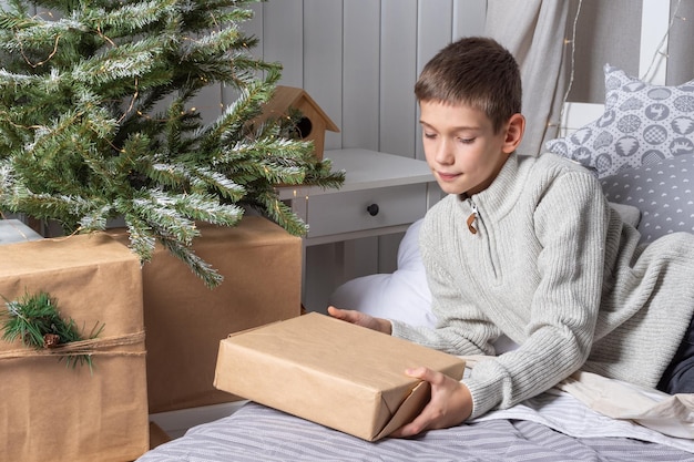 Un lindo adolescente con un suéter saca regalos de debajo de un árbol de Navidad La mañana de Año Nuevo Regalos familiares de Navidad