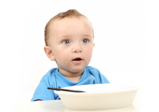 Lindo adorable bebé de un año con ojos verdes comiendo en la mesa, cuchara y plato