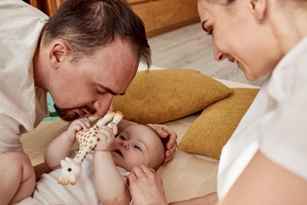 Un lindo y alegre bebé y sus padres yacen en el suelo en una luminosa y acogedora habitación con juguetes que mamá y papá abrazan