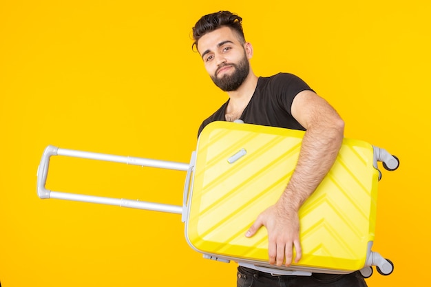 Lindo bastante joven árabe con barba sosteniendo una maleta amarilla en sus manos sobre un amarillo