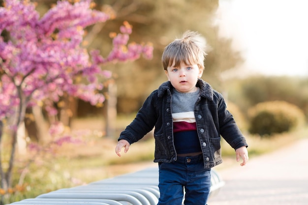 Un lindo bebé de 1 a 2 años usa una chaqueta de mezclilla informal y pantalones posando en el parque al aire libre sobre la naturaleza