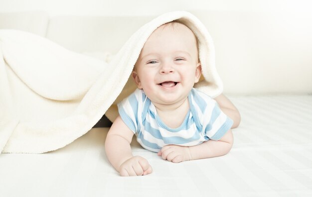 Lindo bebé de 6 meses riendo acostado debajo de la manta en la cama