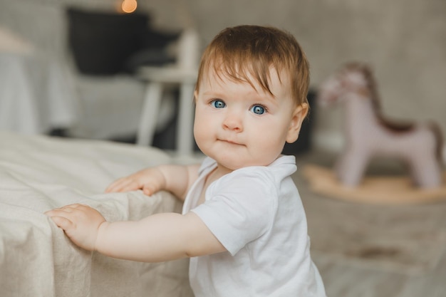 Un lindo bebé de 69 meses está parado cerca de la cama