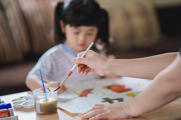 Lindo bebé asiático sonriendo y su mamá madre pintando con pinturas de colores usando acuarela Chica asiática usando pincel de dibujo color Concepto de estilo de vida de actividad de bebé