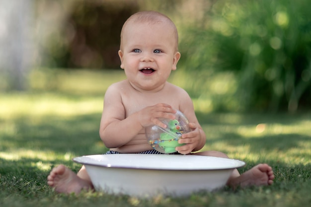 Lindo bebé caluroso día de verano jugando con una tina de agua en el jardín y sonriendo a la cámara