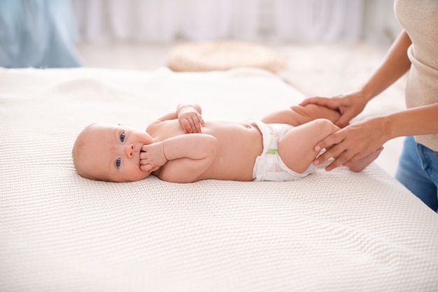 Lindo bebé en la cama con las manos de su madre