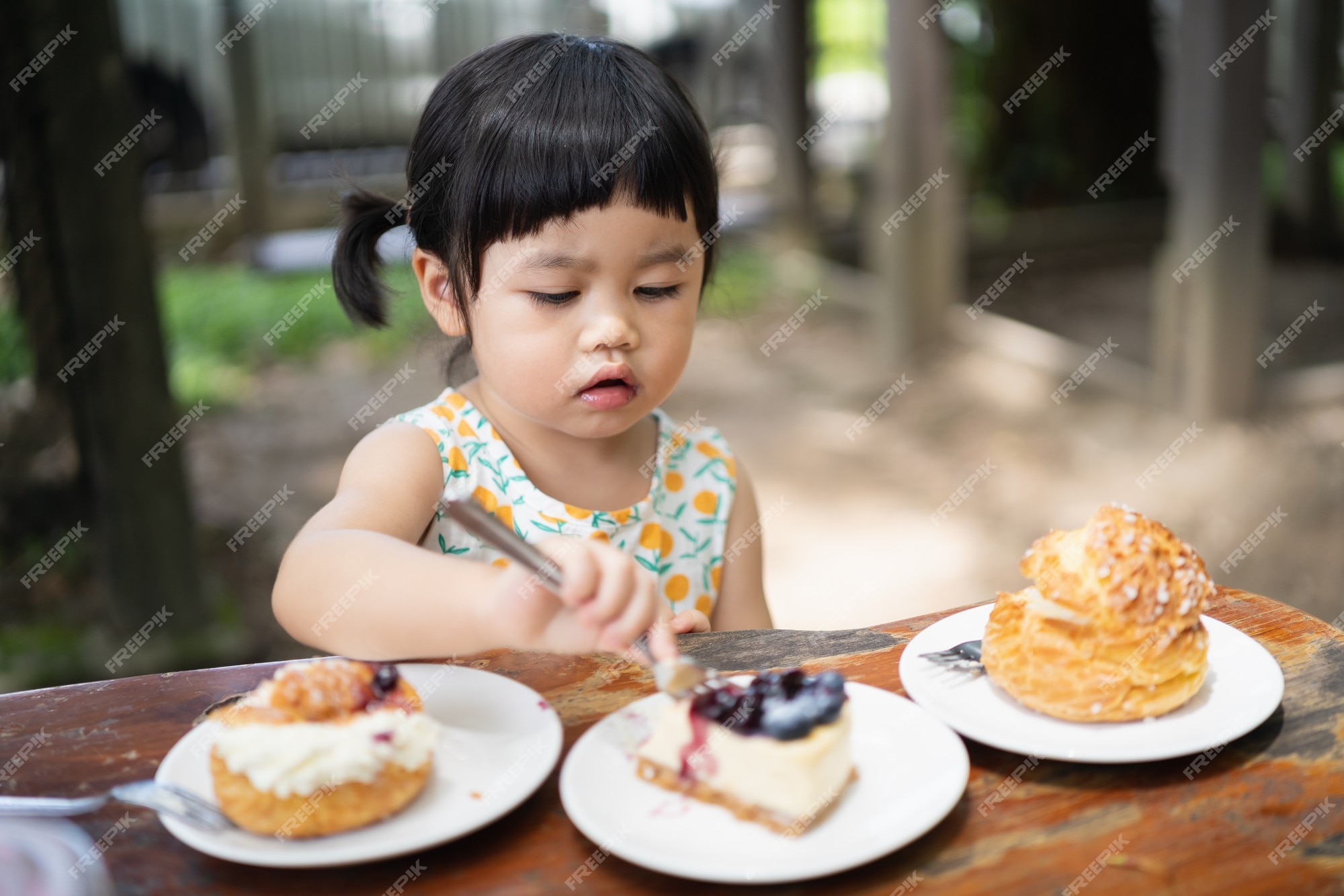 Lindo bebé comiendo pastel y sentado en la mesa del café | Foto Premium