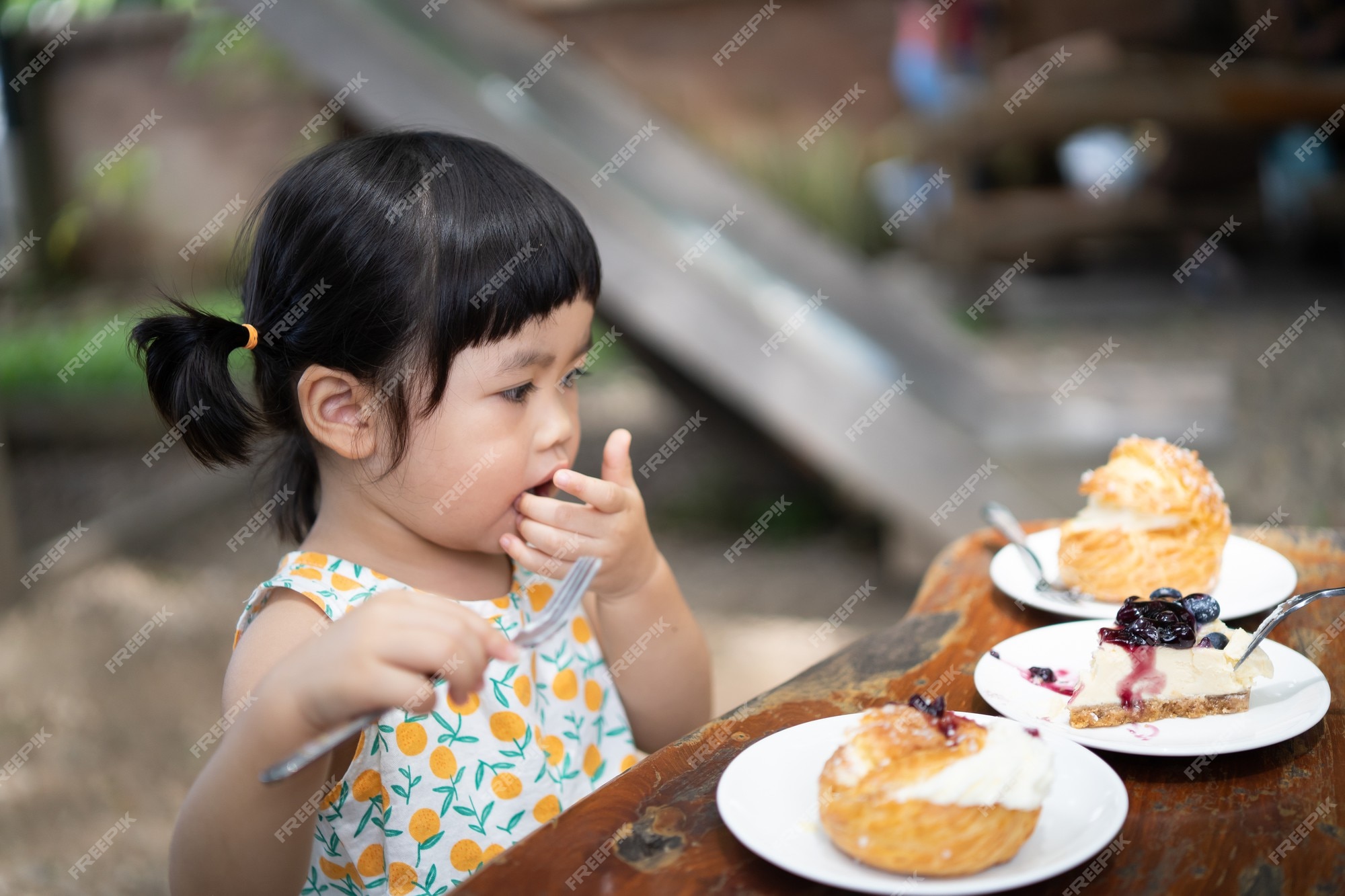 Lindo bebé comiendo pastel y sentado en la mesa del café | Foto Premium