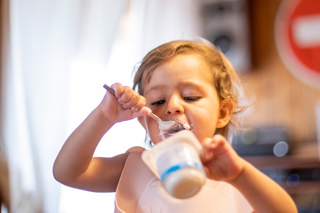 lindo bebé comiendo yogur con cuchara solo. adorable niño tiene el almuerzo. niño hambriento comida fácil